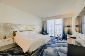 Ein Hotelzimmer mit einem großen Bett, einem Schreibtisch mit Lampe, einem Sessel und einem Fernseher.