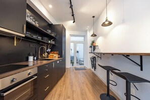 A modern kitchen with dark cabinetry, stainless steel appliances, and a wooden countertop. There is a bar area with stools and pendant lighting. - Stylish 4BR Home in Antwerp Centre | Sleeps 9 Guests (Antwerp)