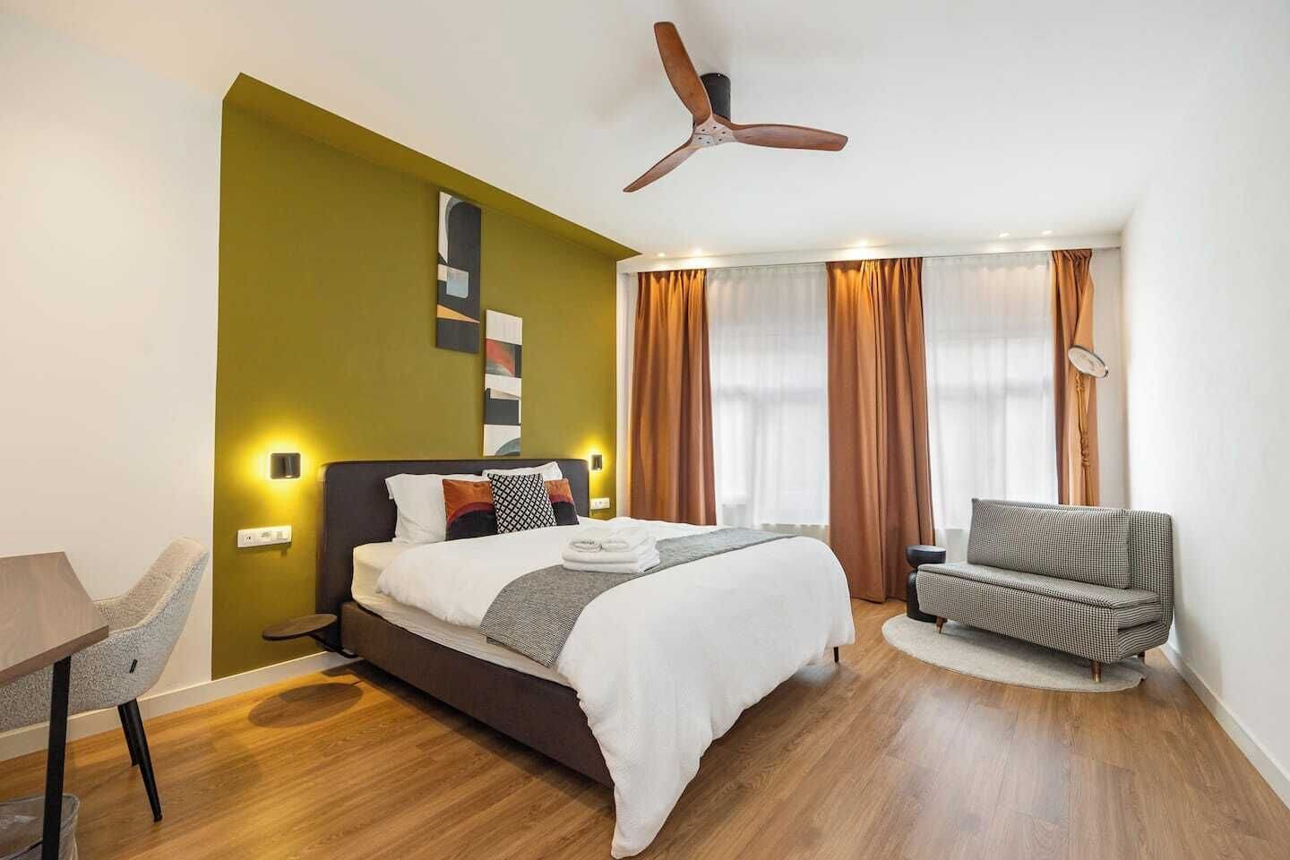 Een hotelkamer met een bed, een stoel, een bureau en een plafondventilator.