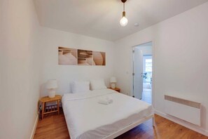 Une chambre à coucher avec un lit, deux tables de chevet avec des lampes, un luminaire au plafond et un radiateur.