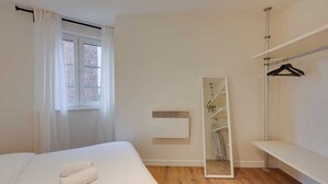 Een slaapkamer met een bed, gordijnen voor het raam, een spiegel, een radiator en een kledingkast.