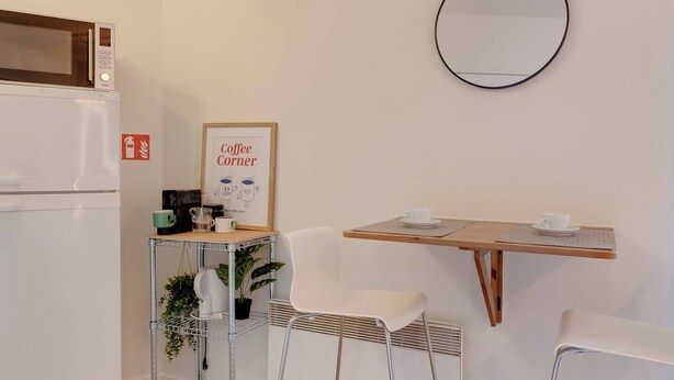 Een compacte kitchenette met een koelkast, een koffiehoek en een spiegel aan de muur.