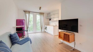 Ett modernt vardagsrum med en soffa, en platt-TV och ett köksområde i bakgrunden.