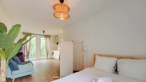 Ett hotellrum med en säng, en sittgrupp med en stol, en stor växt och utsikt över omgivningarna.