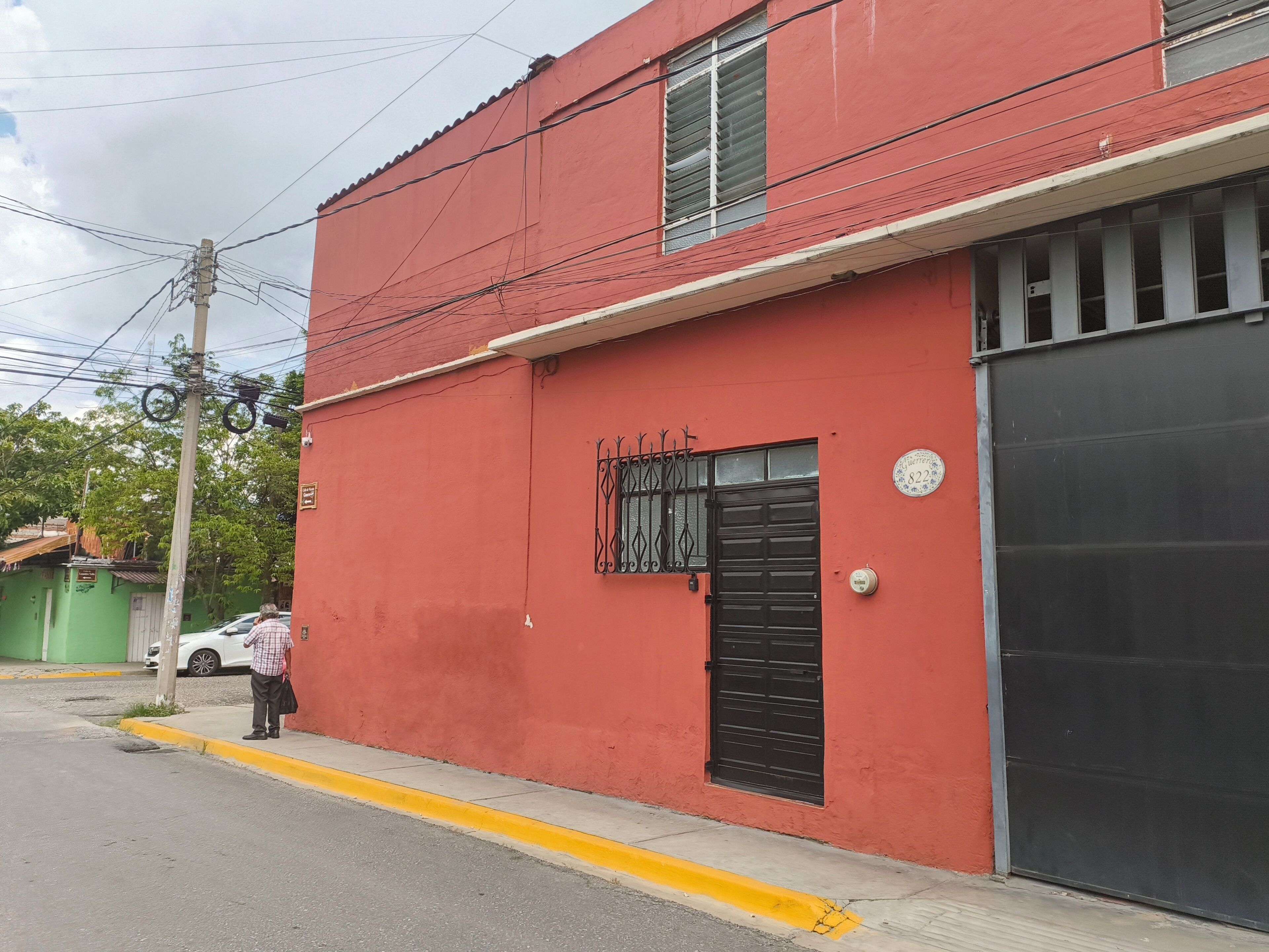 Un bâtiment rouge avec une porte de garage noire, un portail en métal et une petite fenêtre ornée d’une grille métallique.