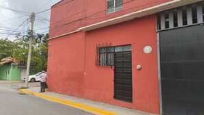 A red building with a black garage door, a metal gate, and a small window with a metal grill. - Oaxaca Loft (Oaxaca de Juárez)