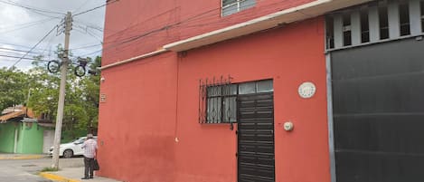 Un bâtiment rouge avec une porte de garage noire, un portail en métal et une petite fenêtre ornée d’une grille métallique.