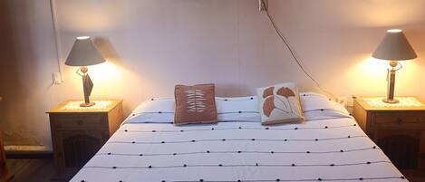 A neatly made bed with a patterned bedspread, two bedside lamps, a wall-mounted light fixture, and a small wooden nightstand with a lamp.