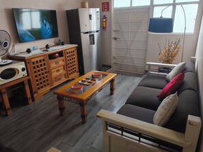 A living room with a TV, wooden furniture, a sofa, and a window with a view. - Oaxaca Loft (Oaxaca de Juárez)