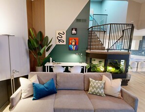 Ein modernes Wohnzimmer mit einer Couch, einem Esstisch und einer Treppe, die in eine obere Ebene führt.