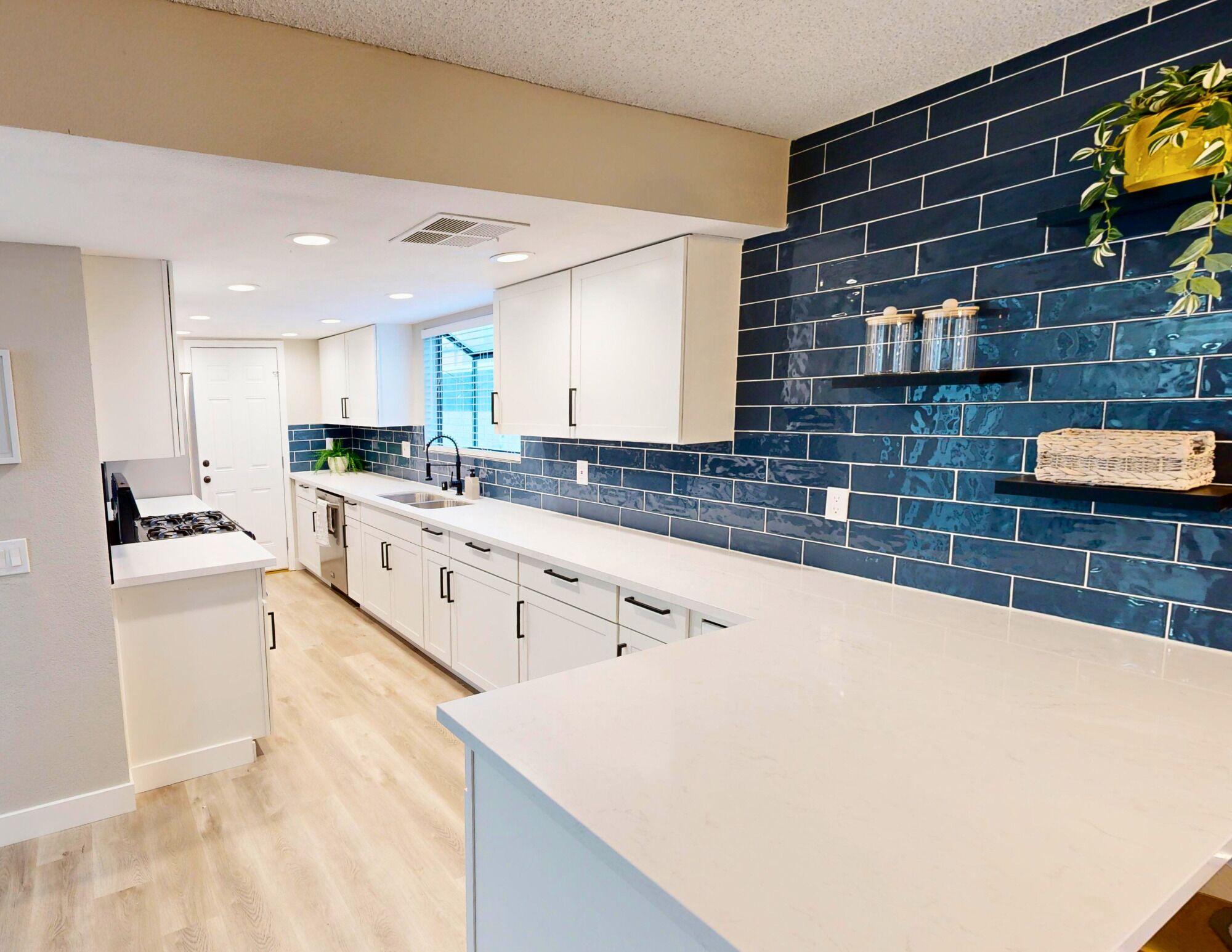 Een moderne keuken met witte kastjes, een blauwe spatwand en een roestvrijstalen spoelbak.