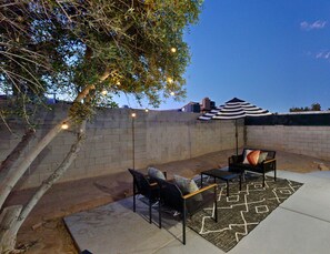 Eine Terrasse im Freien mit Backsteinmauer, Tisch und Stühlen, einem gemusterten Teppich und Lichterketten.
