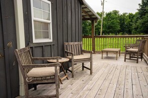 Eine Holzterrasse mit zwei Stühlen, einem Tisch, einem Fenster und Blick auf eine grüne Landschaft.