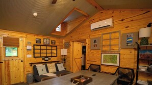 Interior acogedor de una cabaña con una mesa de comedor, sillas, chimenea y un aire acondicionado instalado.