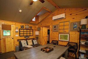 Ein gemütliches Blockhaus-Interieur mit Esstisch, Stühlen, Kamin und Wand-Klimaanlage.