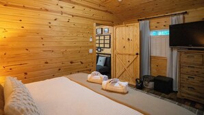 Una habitación de cabaña de madera con una cama, un televisor, un aparador y una ventana con cortinas.