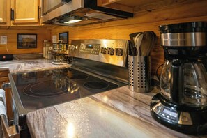 Een keuken met een roestvrijstalen fornuis, een koffiezetapparaat en een pannenhouder.