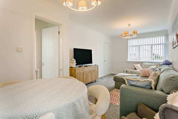 A well-lit room with a television, a sofa, a bed, and a window with blinds.