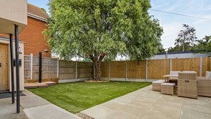 A backyard with a lawn, a wooden fence, a tree, and outdoor furniture.