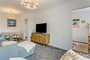 Una sala moderna con un televisor de pantalla plana sobre un mueble de madera, un sofá, una mesa de comedor con sillas y obras de arte en las paredes.