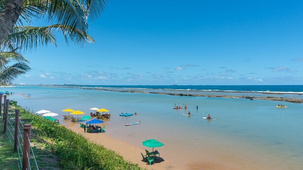 Una playa con agua cristalina, sombrillas y gente disfrutando de actividades acuáticas.