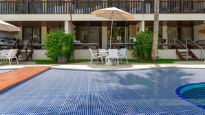 Un área de piscina con suelo de baldosas, mobiliario exterior y un porche cubierto.