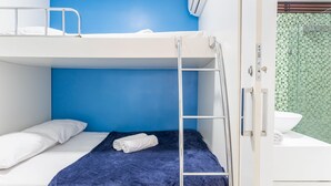 Habitación con literas, pared azul, lavamanos blanco y zona de ducha con azulejos verdes.
