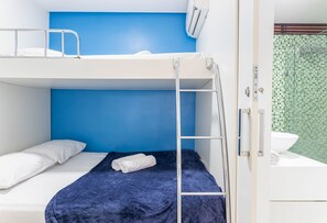 Ett rum med en våningssäng, en blå vägg, ett vitt handfat och en duschhörna med gröna kakelplattor.