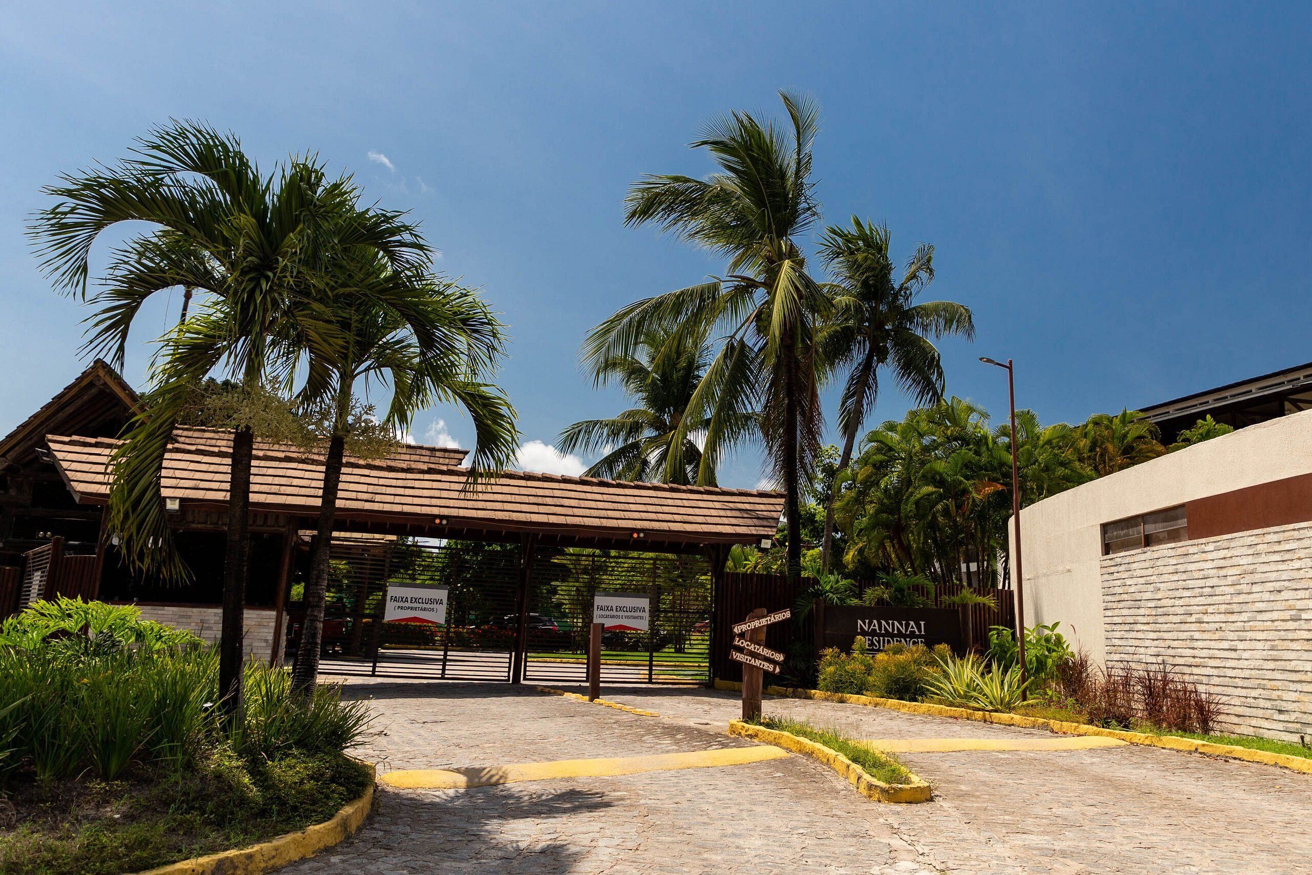 A gated entrance with palm trees, a covered walkway, and a building labeled 'NAUNAI RESIDENCE'.