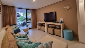 Un salón moderno con un televisor de pantalla plana, un sofá con cojines estampados, una mesita de centro y vistas a una zona de piscina al aire libre.