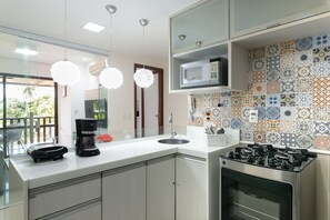 A modern kitchen with a built-in microwave, a coffee maker, and a gas stove. - Nannai Residence Muro Alto Beira Mar (Ipojuca)