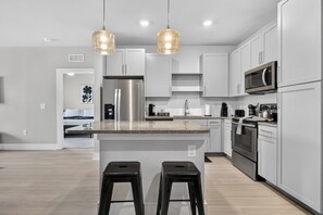 A modern kitchen with stainless steel appliances, a granite countertop, and pendant lighting. - Awesome 2BR Apt/Pool/Gym/King Bed/Beachwalk access (St. Johns)