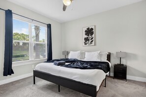 A bedroom with a bed, two bedside tables, a window with blinds, and a ceiling fan. - Awesome 2BR Apt/Pool/Gym/King Bed/Beachwalk access (St. Johns)