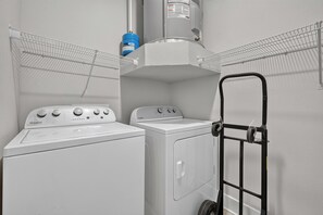 Un área de lavandería con dos lavadoras Whirlpool, un calentador de agua azul y un carro de lavandería negro.