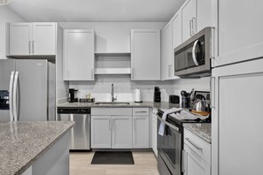 Cocina moderna con armarios blancos, electrodomésticos de acero inoxidable y encimera de granito.