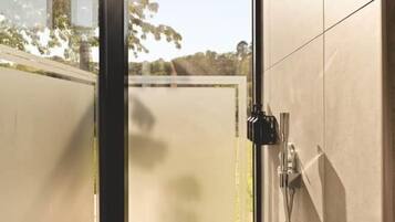 A modern bathroom with a glass door leading to a garden, a shower area, and a toilet.