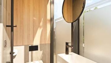 A modern bathroom with a wooden vanity, a round mirror, and a toilet.