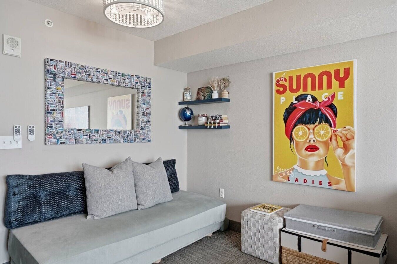Een moderne woonkamer met een grijze bank, een decoratieve spiegel, een plank met kleine objecten en een poster aan de muur.