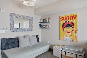 A modern living room with a grey sofa, a decorative mirror, a shelf with small items, and a poster on the wall.
