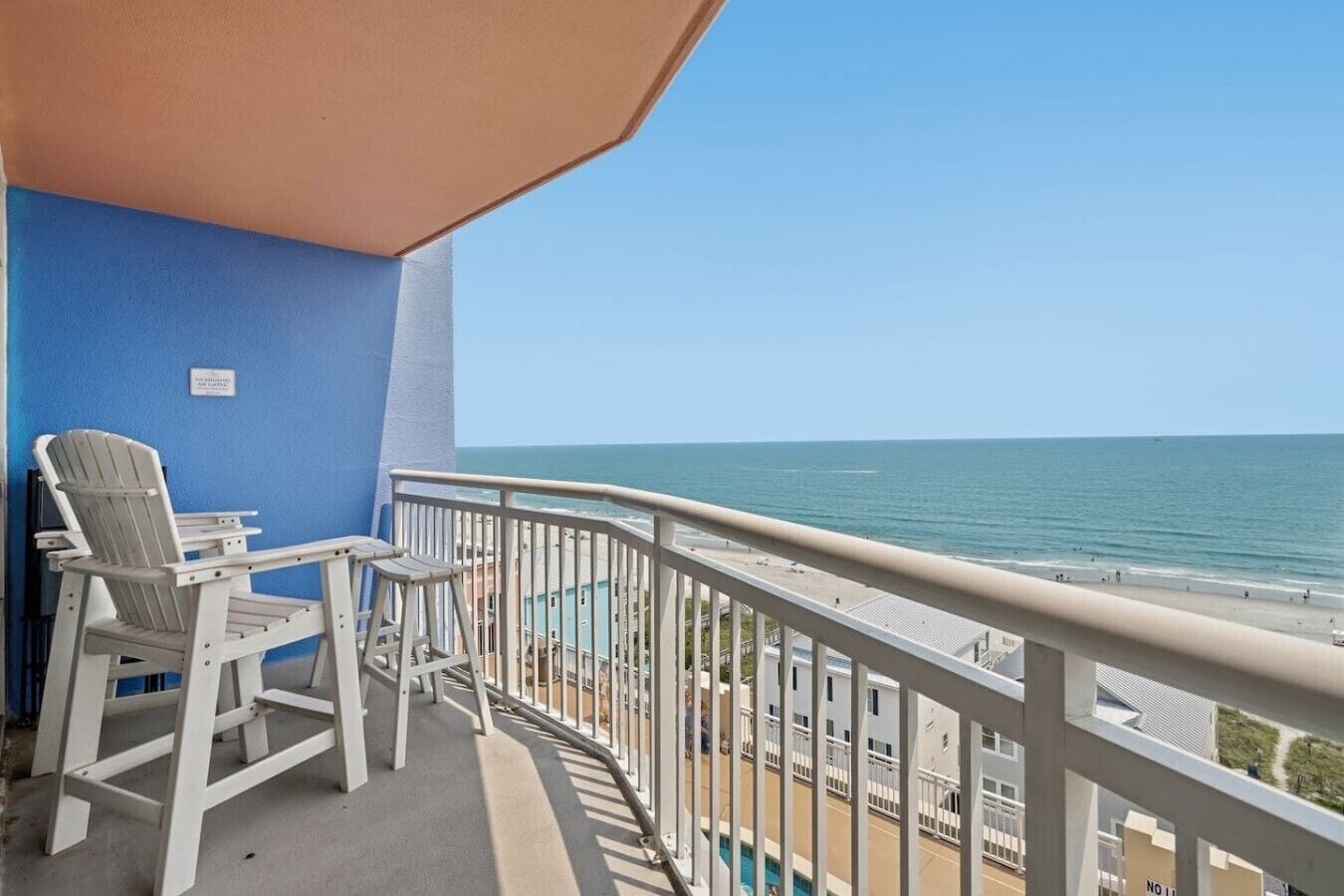 Een balkon met uitzicht op de oceaan, een witte Adirondack-stoel en een kleine tafel.