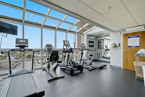 A gym with various exercise machines, a large window with a city view, and a door with a sign.