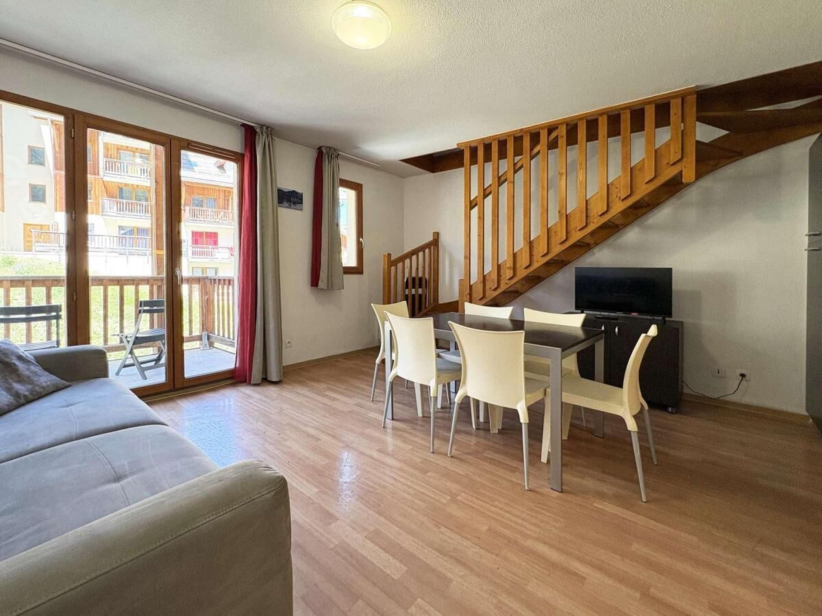 A living room with a wooden staircase, a sofa, a dining table with chairs, and a television.