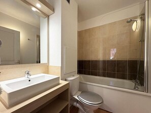 Une salle de bain avec un lavabo blanc, des toilettes et une douche fermée par une paroi de verre.