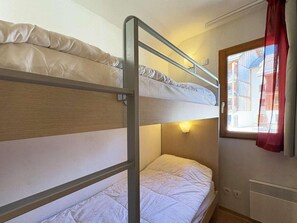 Une chambre avec un lit superposé, une fenêtre et un radiateur.