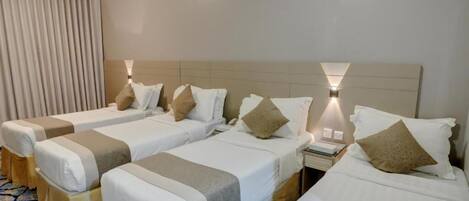 Quarto de hotel com duas camas de solteiro, uma mesa de cabeceira, uma luminária e uma janela com cortinas.