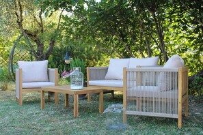 Eine hölzerne Außenlounge mit zwei Sofas und einem Tisch, umgeben von viel Grün.