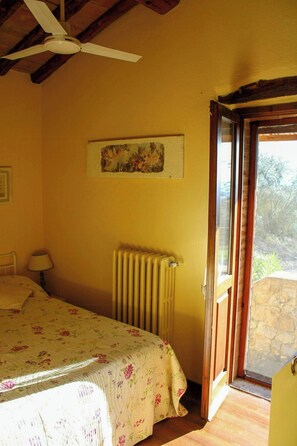 Ein Schlafzimmer mit Bett, Heizkörper, Deckenventilator, einem Gemälde und einer Tür zu einem Außenbereich.
