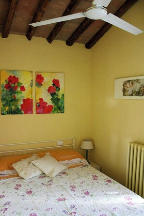 A bedroom with a bed, a ceiling fan, two paintings, a bedside lamp, and a radiator. - Shabby chic cottage with pool in Chianti (Castellina in Chianti)