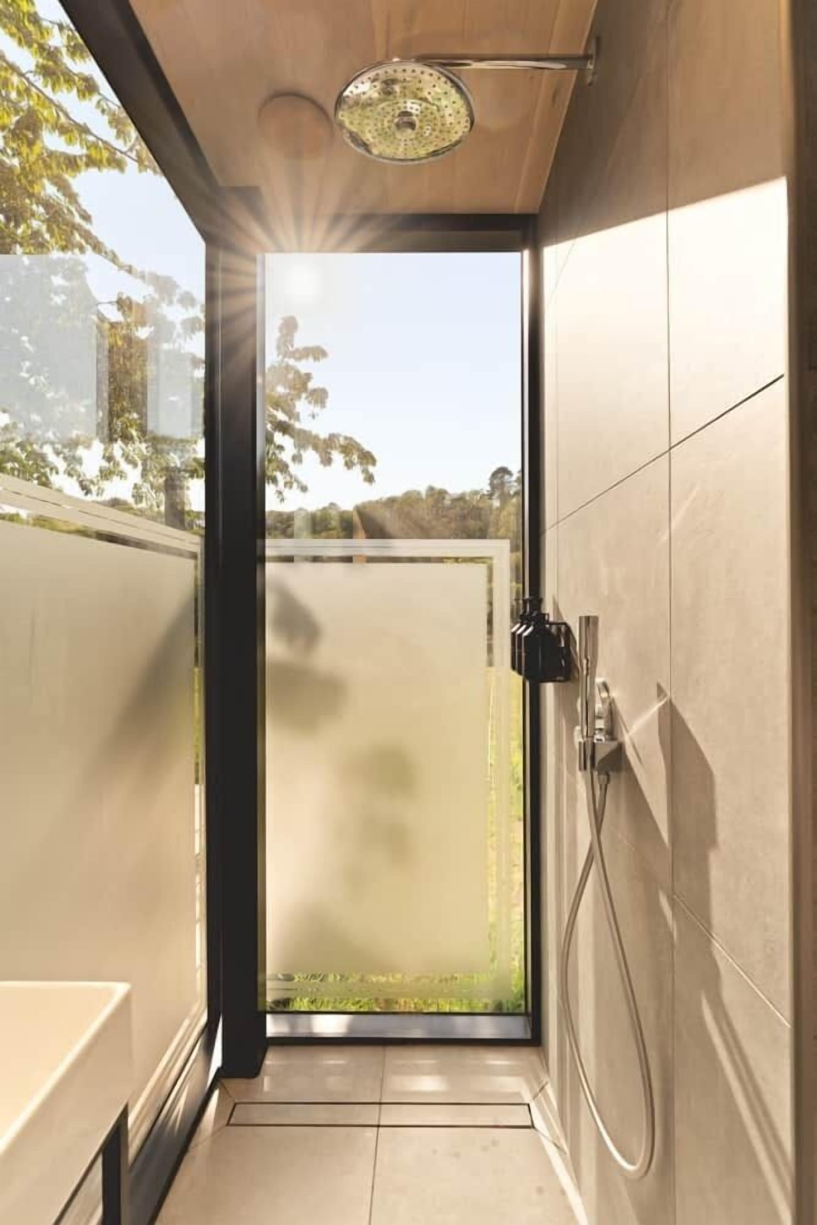 A modern bathroom with a glass door leading to a garden, a shower area, and a toilet.