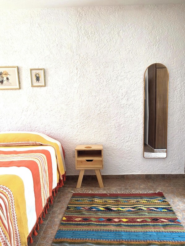 A bedroom with a bed, a small wooden nightstand, a mirror, and a colorful rug. - A great location with contemporary comfort and the richness of Oaxacan culture. (Oaxaca de Juárez)